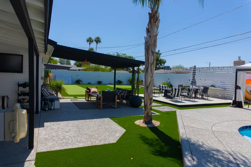 Modern backyard oasis with artificial turf, seating areas, and a pool under a clear blue sky.