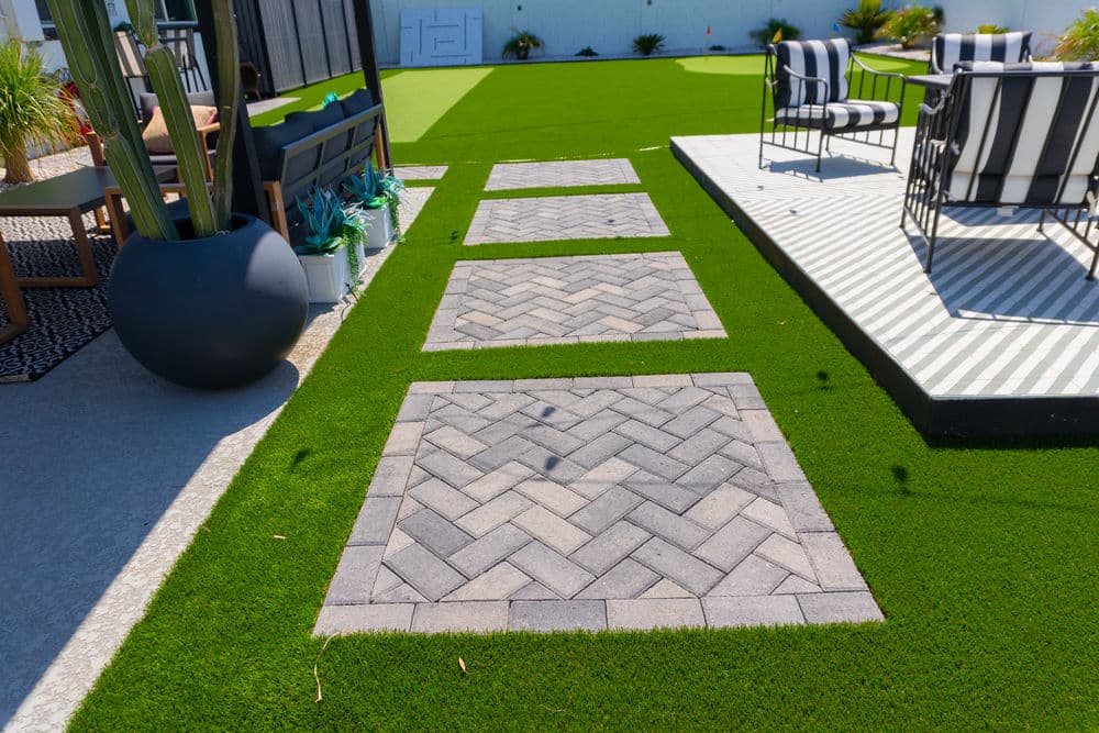 Modern outdoor space with paver pathways on artificial grass, featuring sleek furniture and decor.