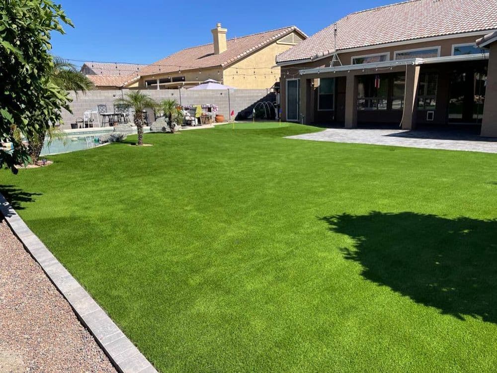 Lush green artificial lawn with a pool and patio area in a residential backyard.