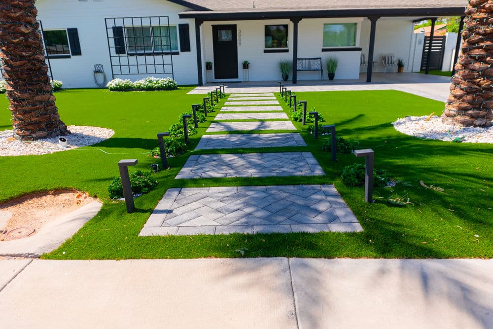 Pathway with pavers lined by modern lights leading to a stylish home surrounded by lush grass.
