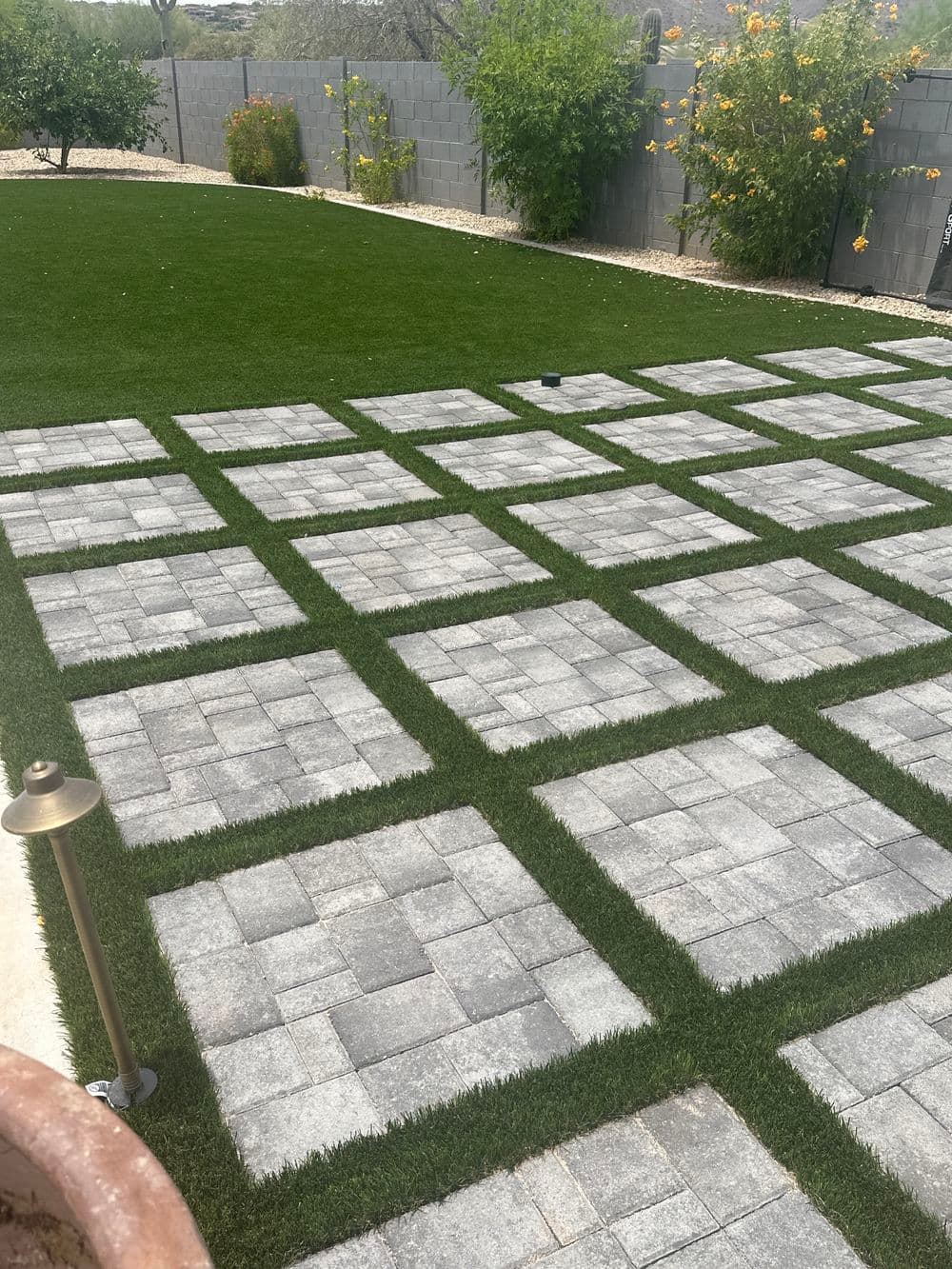 Modern backyard design featuring grassy patches between stone pavers, creating a stylish landscape.