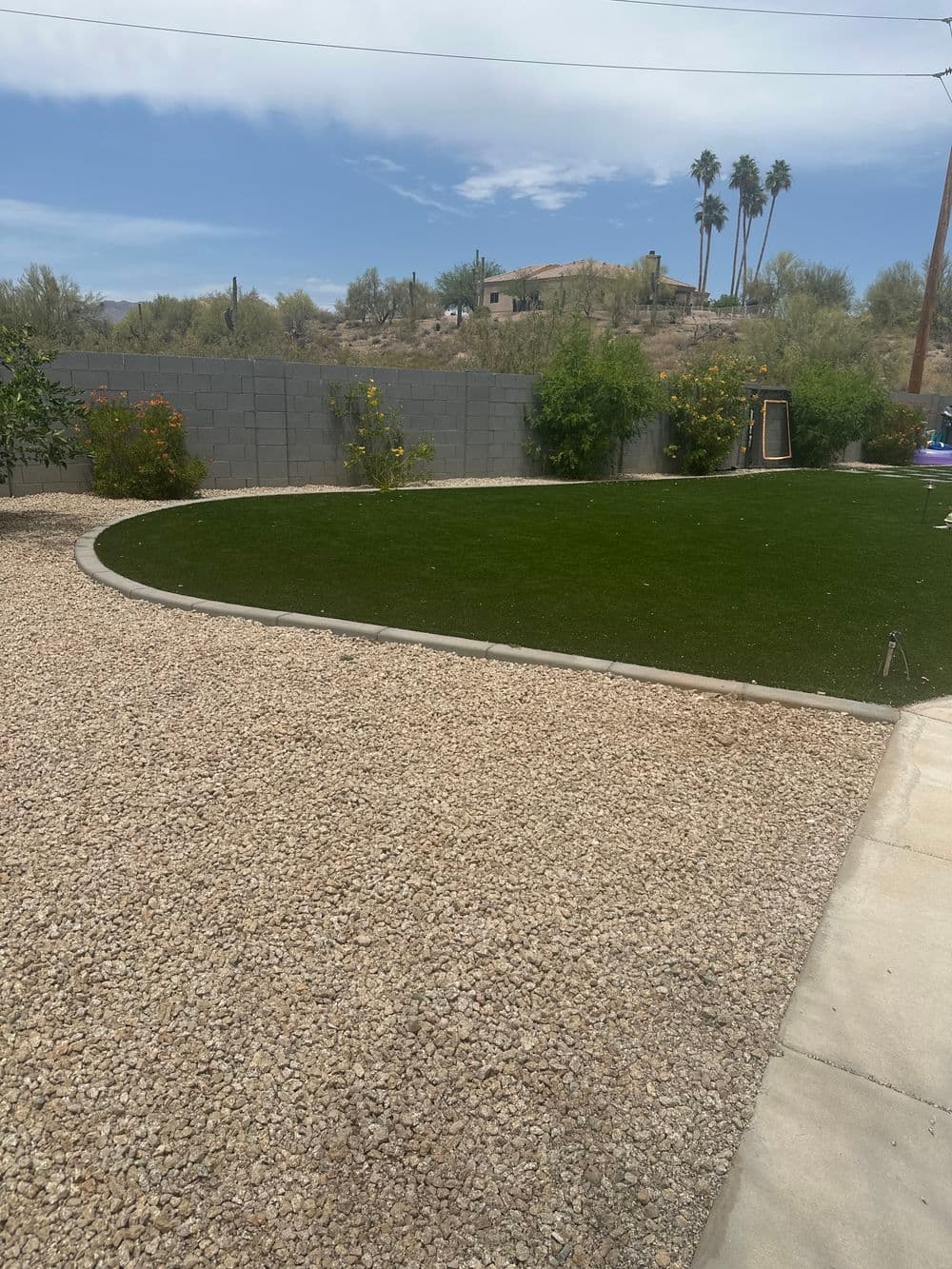Desert landscape with artificial turf, gravel area, and lush shrubs under a blue sky.