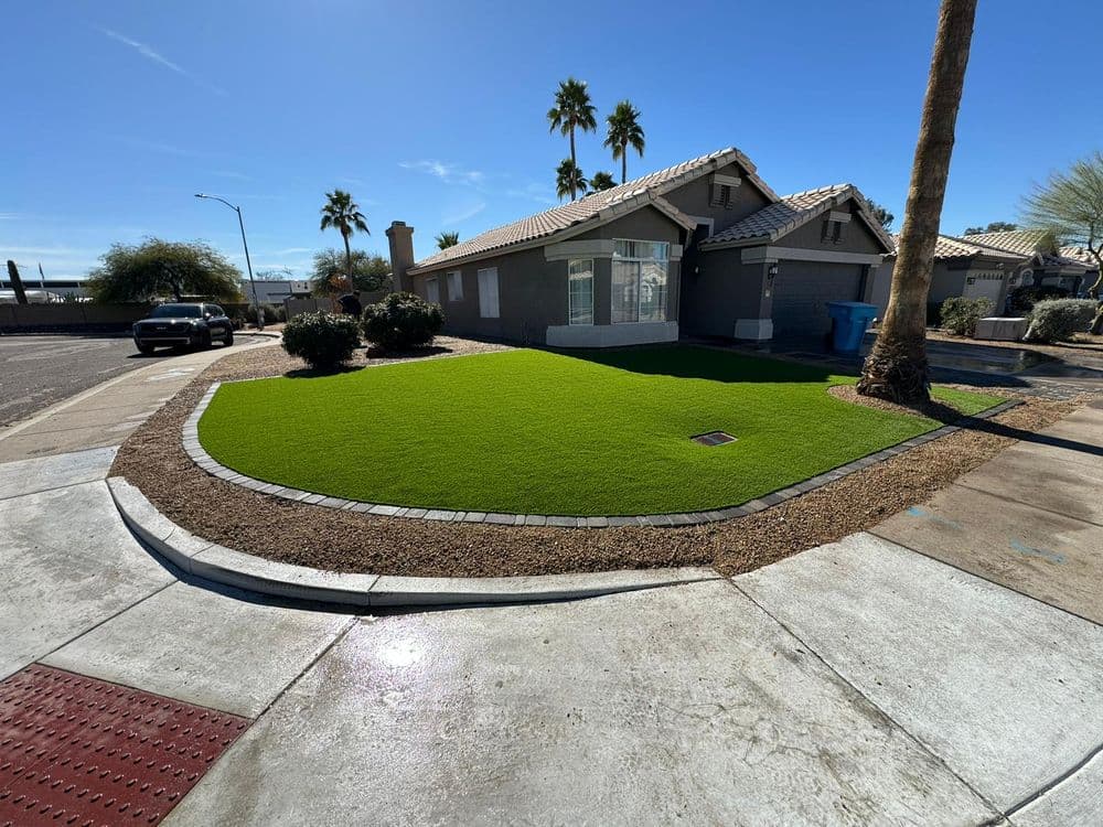 Lush green artificial lawn in front of a suburban house with palm trees and gravel landscaping.