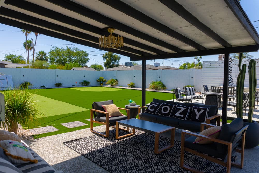 Cozy backyard patio with green grass, lounge seating, and outdoor dining area under a shaded roof.