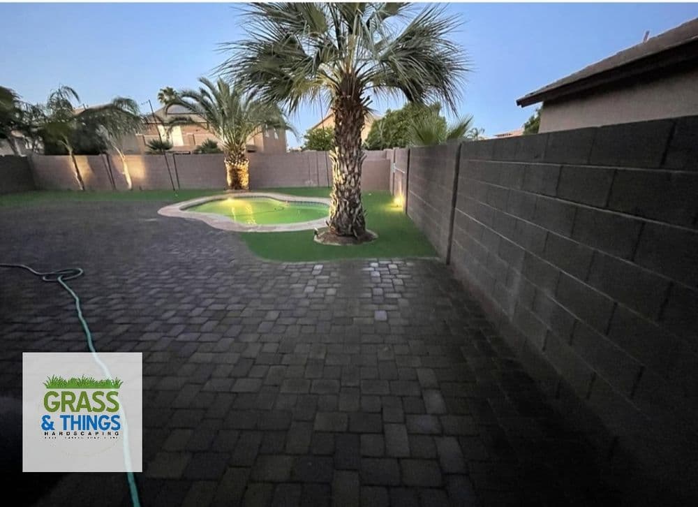 Backyard with palm trees, pool, and paver stones at dusk, illuminated by soft lights.