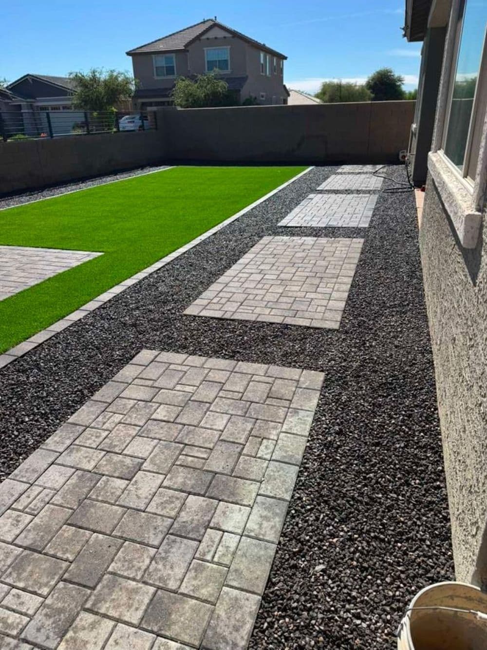 Modern backyard with synthetic grass, stone pathways, and decorative gravel area.