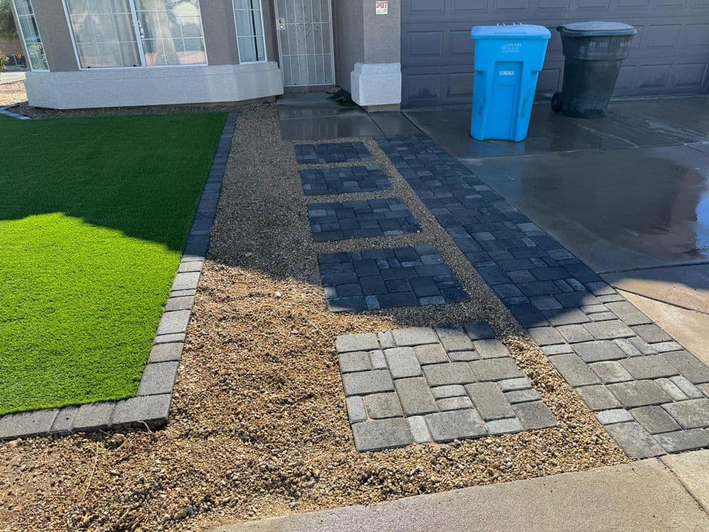 Landscaped yard with paver stones, artificial grass, and trash bins in a residential area.