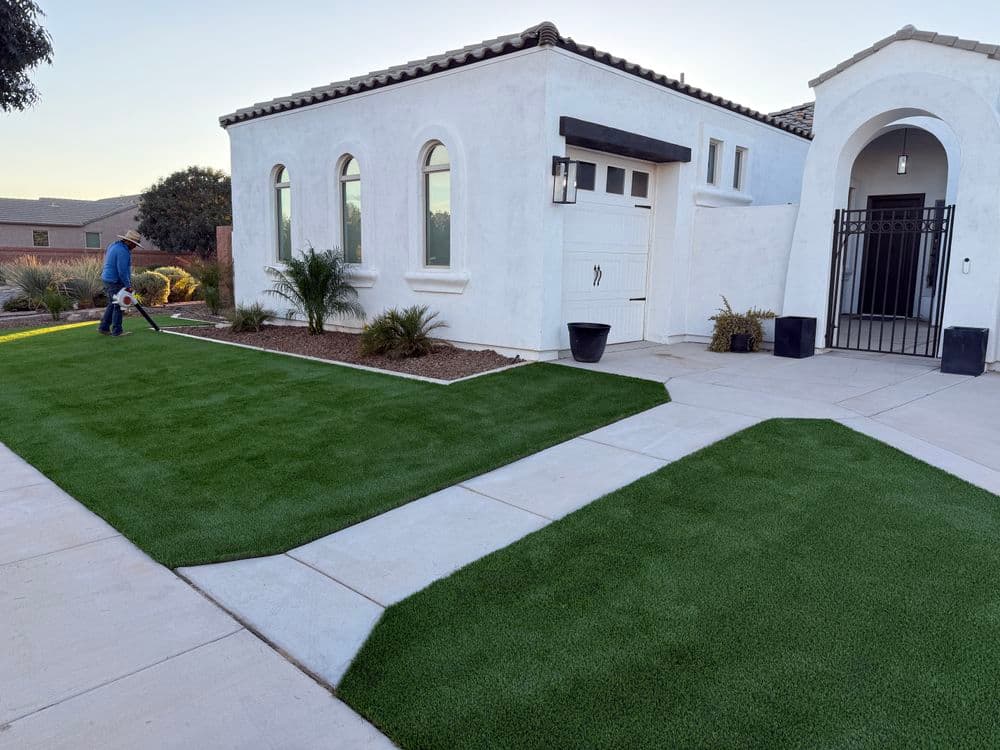 Lush green lawn with modern home exterior and landscaping, featuring a worker maintaining the yard.