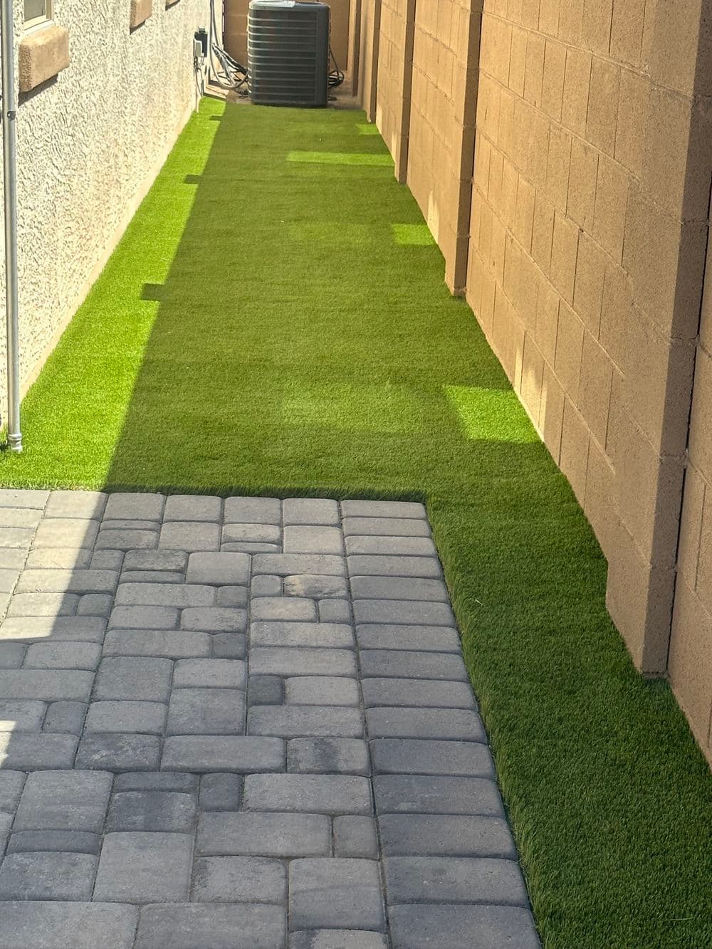 Artificial turf alongside a paved walkway in a residential backyard landscape.