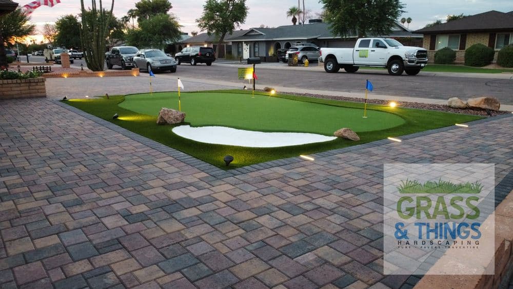 Home putting green installation with artificial turf, landscaped lights, and brick paver pathway.