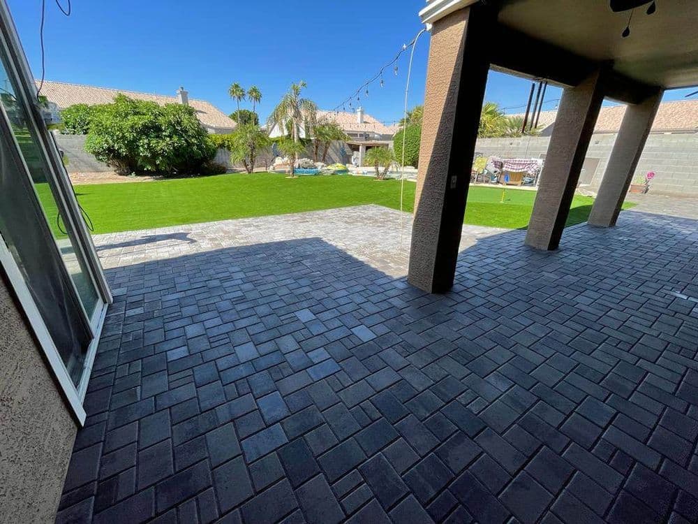 View of a landscaped backyard with paver patio, lawn area, and palm trees under a clear blue sky.