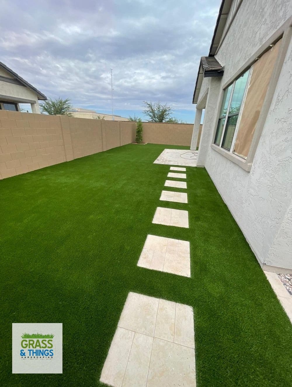 Lush green artificial grass with stone pathway beside a modern house in a sunny neighborhood.