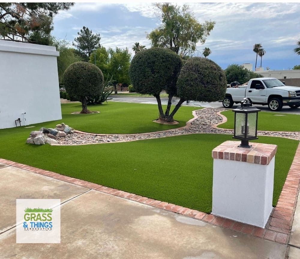 Lush green artificial lawn with decorative rocks, shrubs, and a lantern in a landscaped yard.