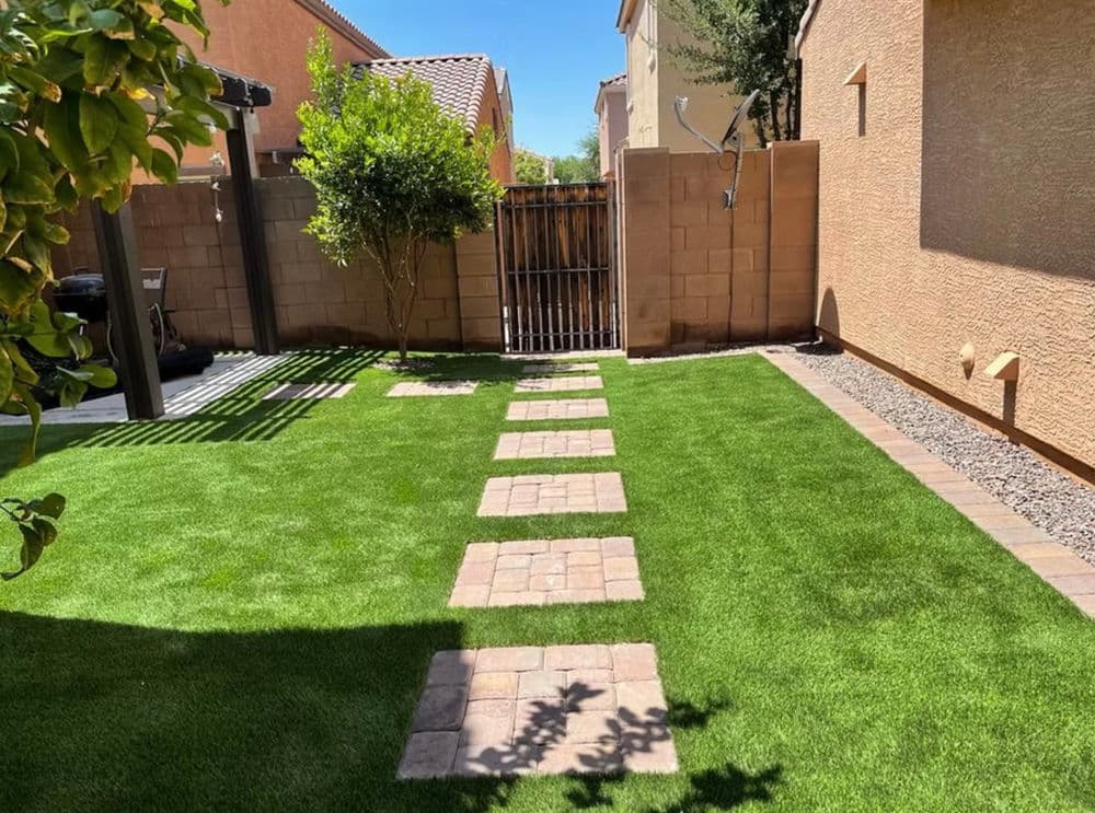 Backyard with green artificial grass, stone pathway, and gated fence in a residential setting.