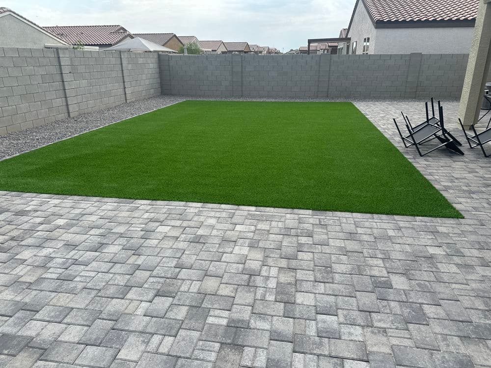 Modern backyard with artificial turf on paver patio, gray walls, and minimal furniture.
