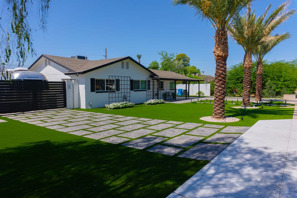 Modern home exterior with palm trees, green lawn, and stone pathway under a clear blue sky.