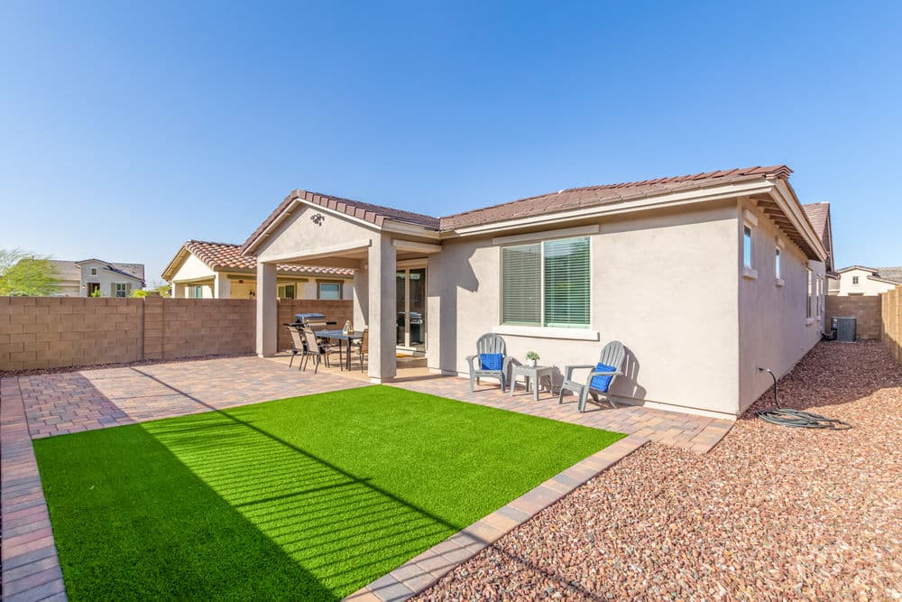Modern home backyard with patio, green turf, and seating area on a sunny day.