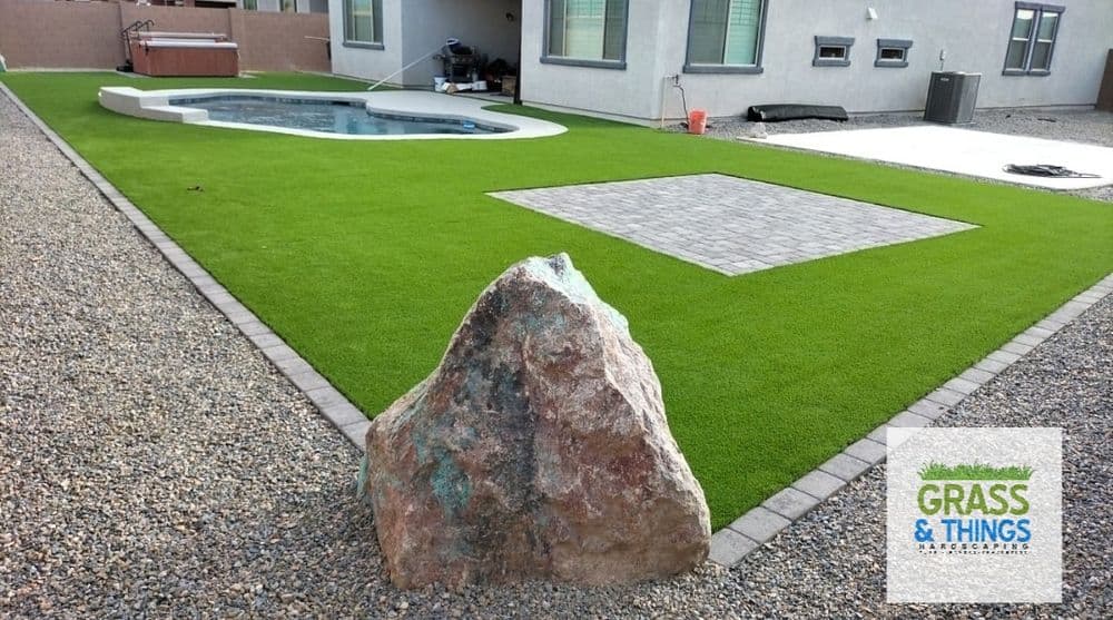 Artificial grass landscape featuring a pool, stone rock, and patio pavers.