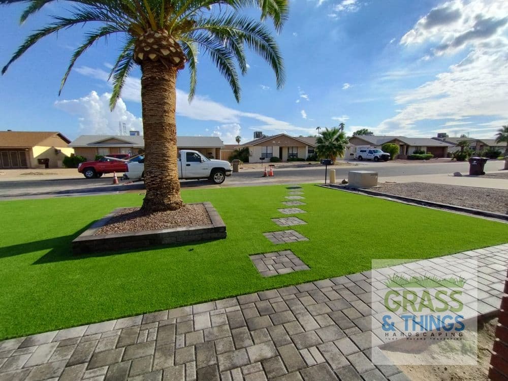 Lush artificial grass landscaping with palm tree and paver walkway in residential area.