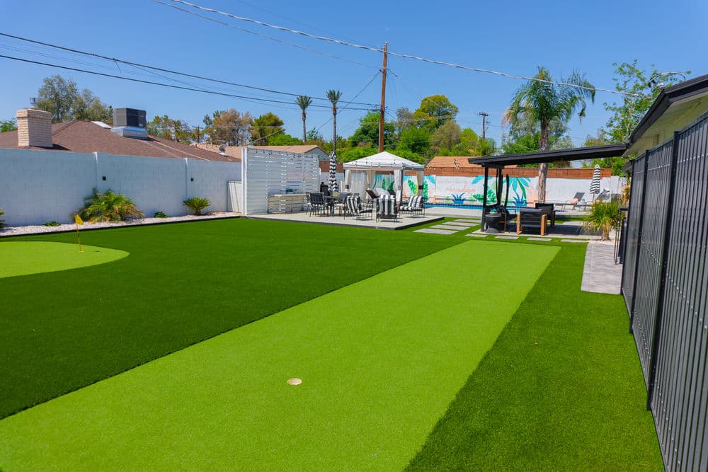 Lush green backyard with artificial turf, patio seating, and decorative wall mural.