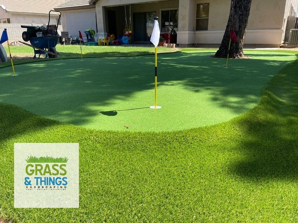 Artificial grass putting green with flags and landscaping tools in a sunny backyard.