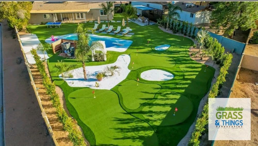 Aerial view of a landscaped backyard with a pool, putting green, and palm trees.